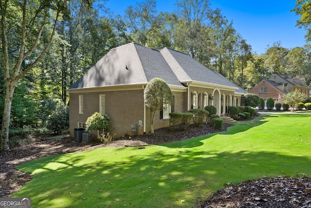 view of front of home featuring roof with shingles, brick siding, central air condition unit, covered porch, and a lawn