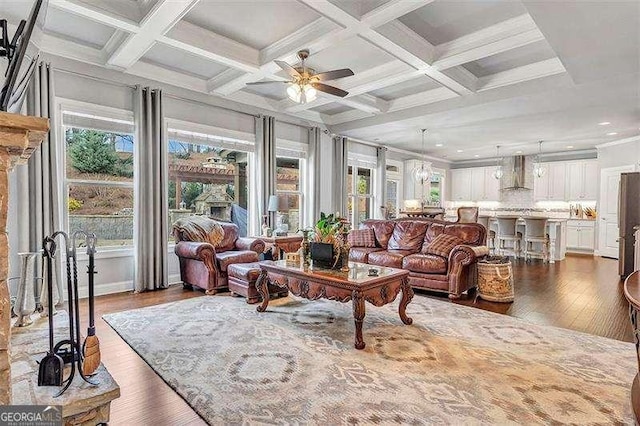 living room featuring ceiling fan with notable chandelier, ornamental molding, coffered ceiling, dark wood-type flooring, and beam ceiling