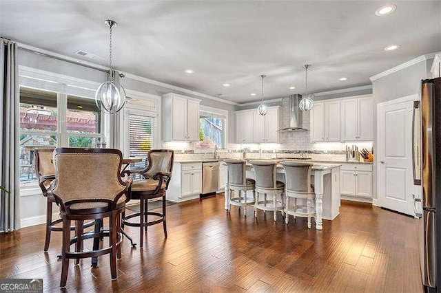 kitchen with hanging light fixtures, white cabinetry, a kitchen island, and wall chimney range hood