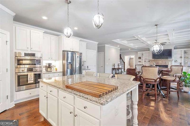 kitchen with white cabinetry, stainless steel appliances, light stone countertops, a kitchen island, and decorative light fixtures