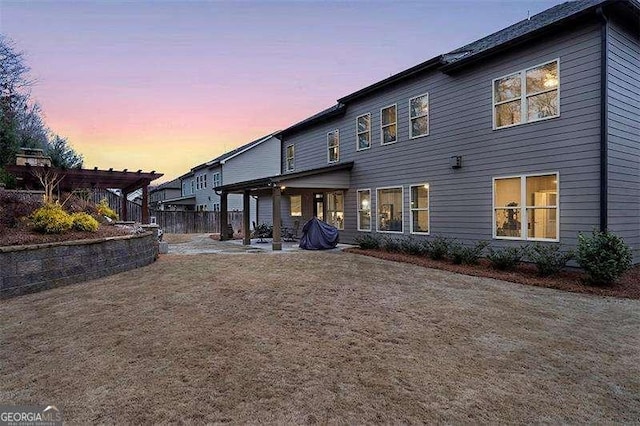 back house at dusk with a pergola and a patio