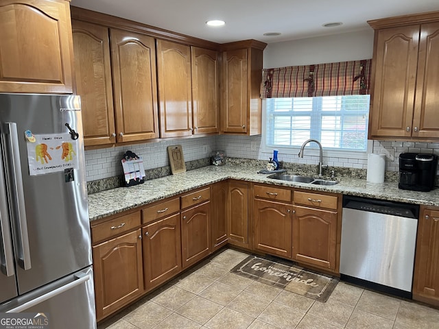 kitchen with appliances with stainless steel finishes, brown cabinetry, a sink, and light stone countertops