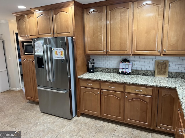 kitchen with tasteful backsplash, appliances with stainless steel finishes, brown cabinets, ornamental molding, and light stone countertops