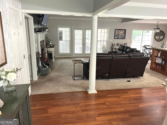 living room featuring crown molding, dark colored carpet, a fireplace with raised hearth, dark wood-type flooring, and ornate columns