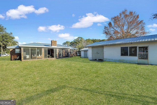 rear view of property with a sunroom, a chimney, metal roof, and a lawn