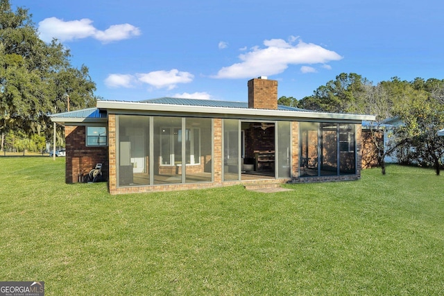 back of house featuring a sunroom, metal roof, a chimney, and a lawn