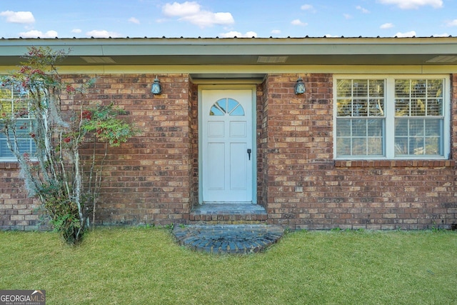 doorway to property with a yard and brick siding