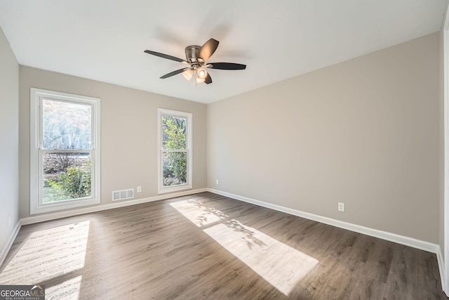 unfurnished room with a ceiling fan, wood finished floors, visible vents, and baseboards