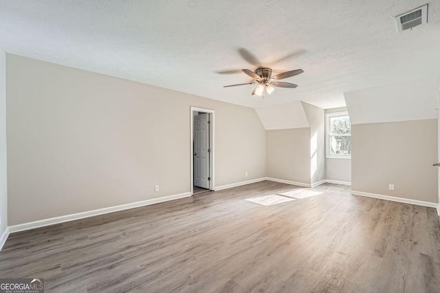 bonus room with dark wood-style floors, lofted ceiling, visible vents, a textured ceiling, and baseboards