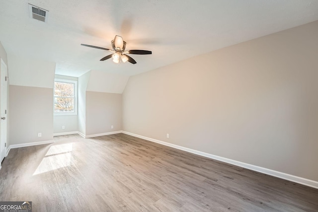 additional living space with ceiling fan, lofted ceiling, wood finished floors, visible vents, and baseboards