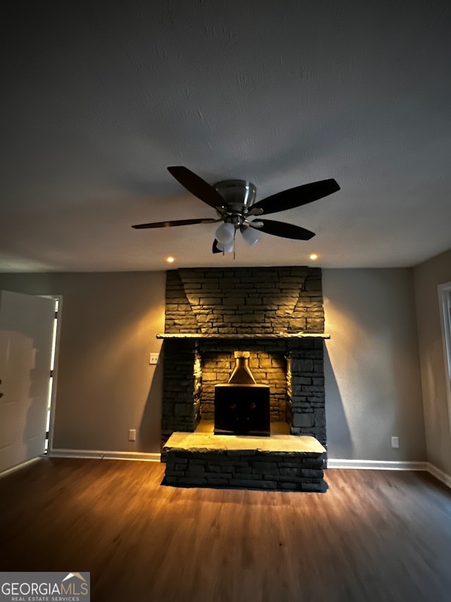 unfurnished living room featuring ceiling fan, a fireplace, baseboards, and wood finished floors