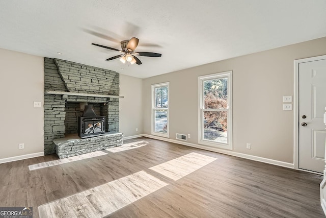 unfurnished living room with visible vents, a ceiling fan, a wood stove, wood finished floors, and baseboards