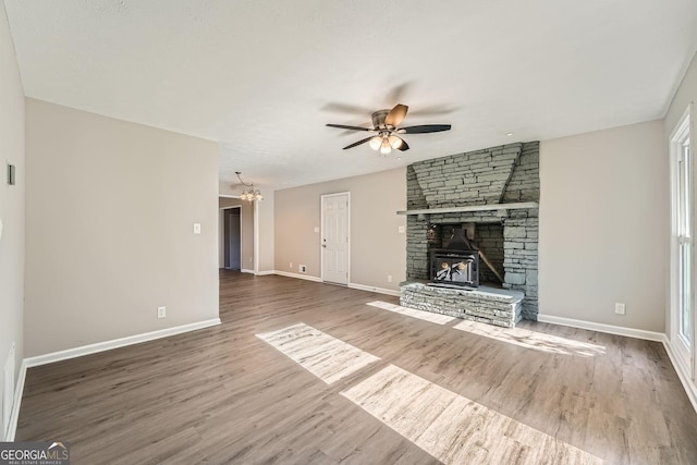 unfurnished living room featuring ceiling fan with notable chandelier, a stone fireplace, baseboards, and wood finished floors