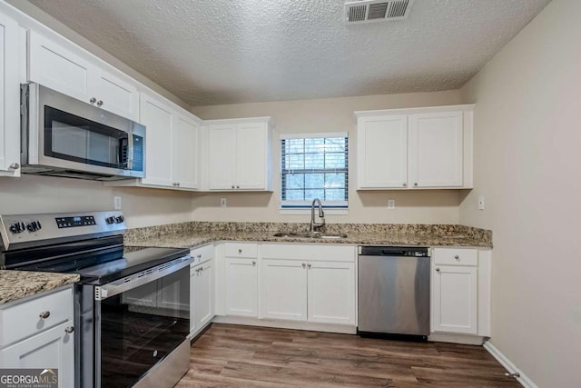 kitchen featuring sink, hardwood / wood-style flooring, stainless steel appliances, light stone counters, and white cabinets