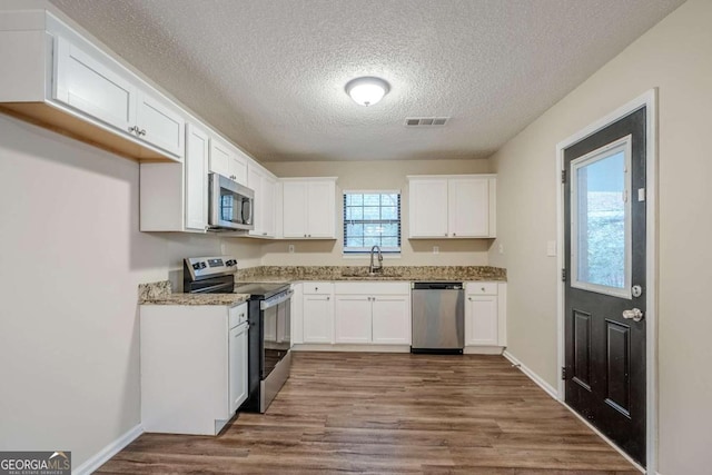 kitchen with appliances with stainless steel finishes, sink, white cabinets, dark hardwood / wood-style flooring, and a textured ceiling