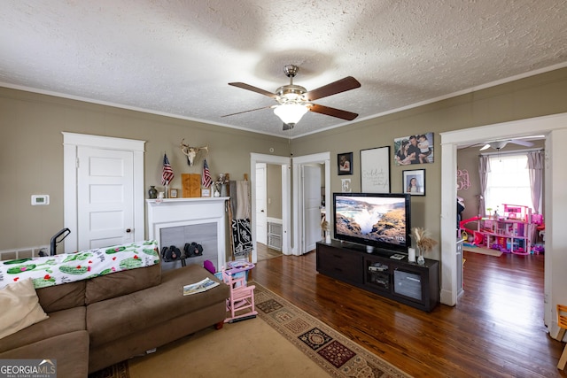 living room featuring a textured ceiling, a tiled fireplace, ceiling fan, crown molding, and dark hardwood / wood-style flooring