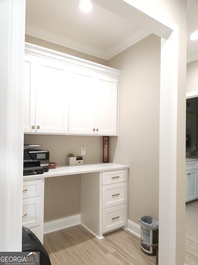 office space featuring crown molding, built in desk, and light hardwood / wood-style floors