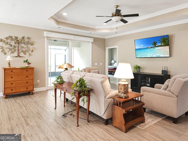 living room with crown molding, ceiling fan, a tray ceiling, and light wood-type flooring