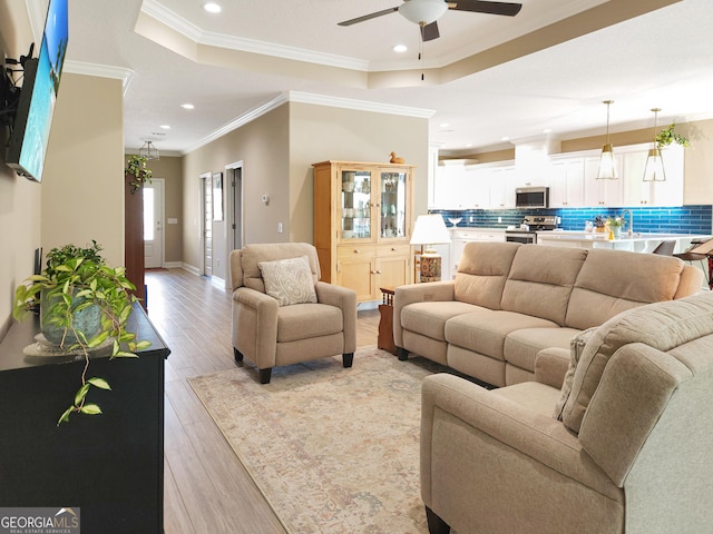 living room with ceiling fan, ornamental molding, a tray ceiling, and light hardwood / wood-style floors