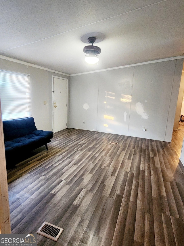 unfurnished living room with a textured ceiling, dark wood-style flooring, visible vents, and crown molding