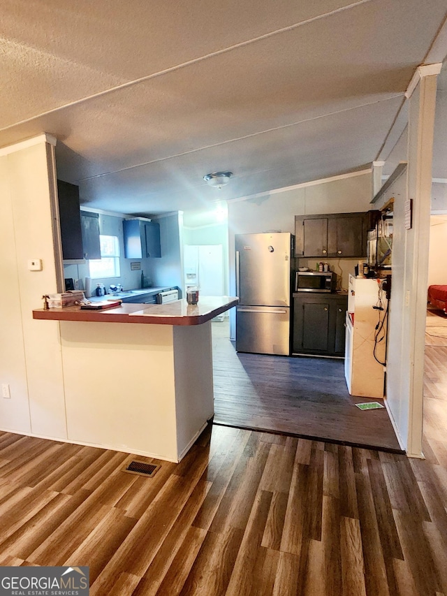 kitchen featuring a breakfast bar, appliances with stainless steel finishes, dark wood-type flooring, a textured ceiling, and a peninsula