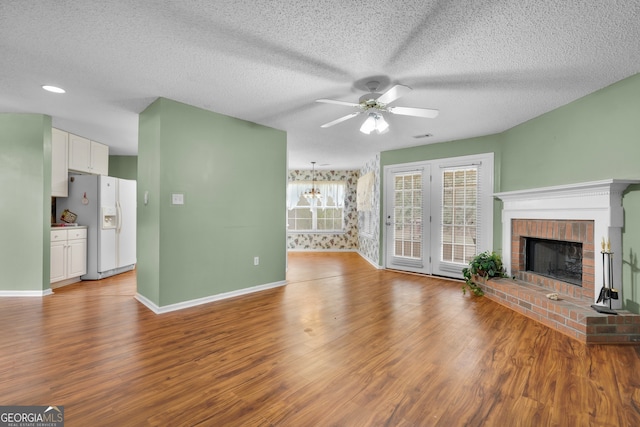 unfurnished living room with ceiling fan, wood-type flooring, a brick fireplace, and a textured ceiling