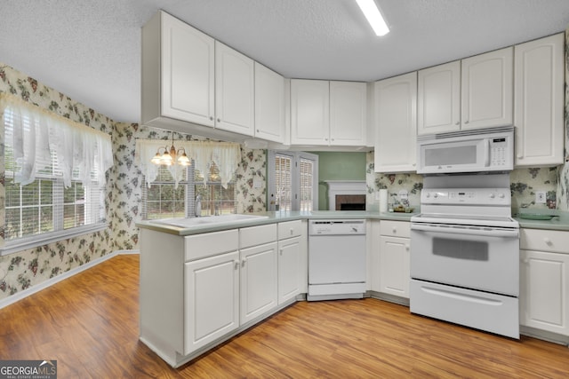 kitchen with white appliances, white cabinetry, a textured ceiling, kitchen peninsula, and light wood-type flooring