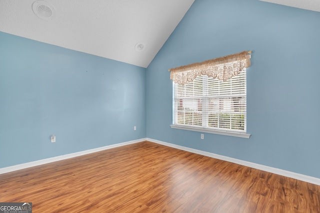 spare room featuring lofted ceiling and hardwood / wood-style floors