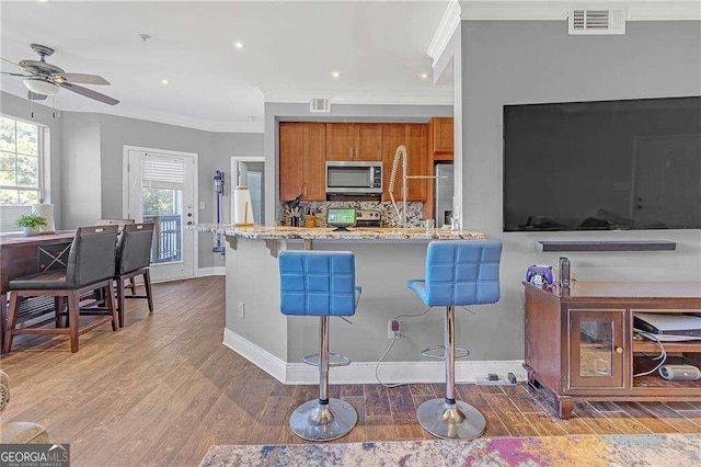 kitchen with hardwood / wood-style flooring, a breakfast bar area, backsplash, stainless steel appliances, and light stone counters