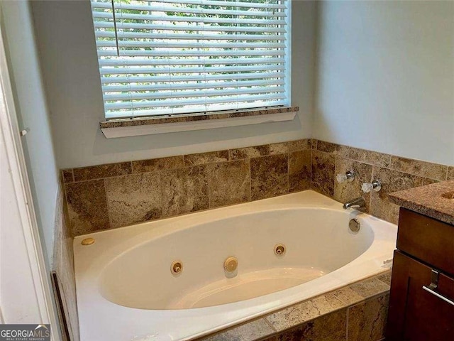 bathroom with vanity, tiled tub, and a healthy amount of sunlight