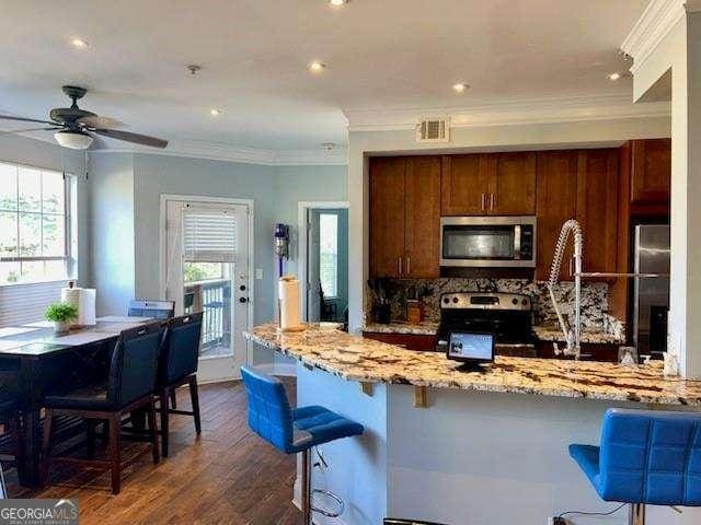 kitchen with a breakfast bar area, appliances with stainless steel finishes, dark hardwood / wood-style floors, light stone counters, and decorative backsplash