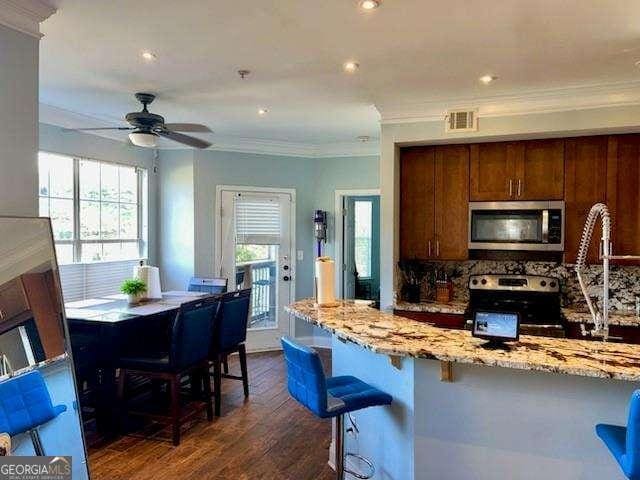 kitchen featuring a kitchen bar, tasteful backsplash, appliances with stainless steel finishes, dark hardwood / wood-style flooring, and light stone countertops