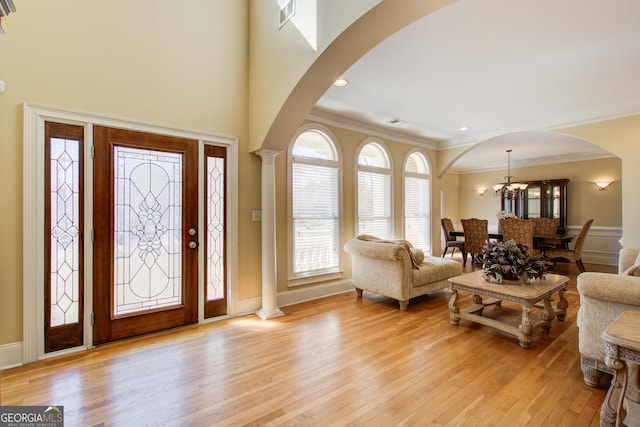 foyer featuring arched walkways, light wood-style flooring, crown molding, and ornate columns