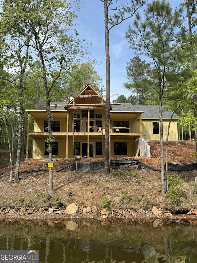 rear view of house featuring board and batten siding, a water view, and roof with shingles
