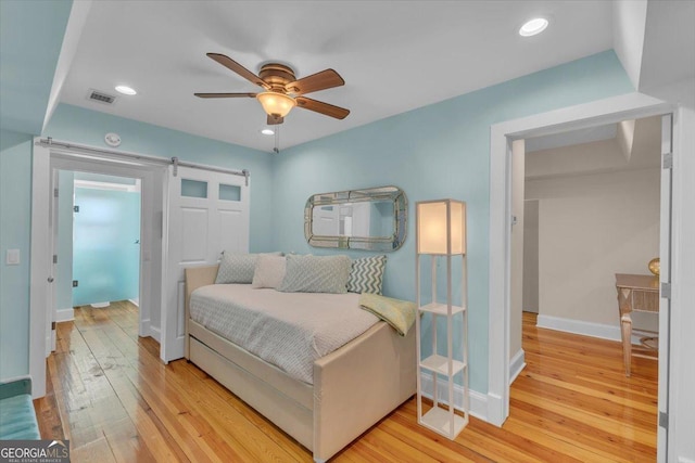 bedroom featuring light hardwood / wood-style floors, a barn door, and ceiling fan