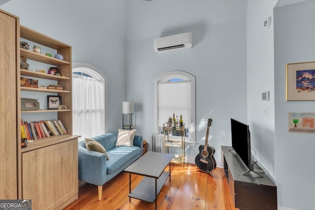 sitting room featuring a towering ceiling, wood-type flooring, radiator, and a wall unit AC