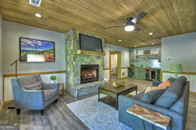 living room featuring bar area, beverage cooler, a stone fireplace, and wooden ceiling