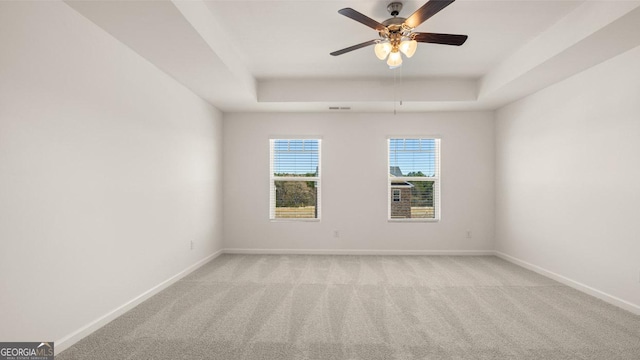 carpeted spare room with a raised ceiling and ceiling fan