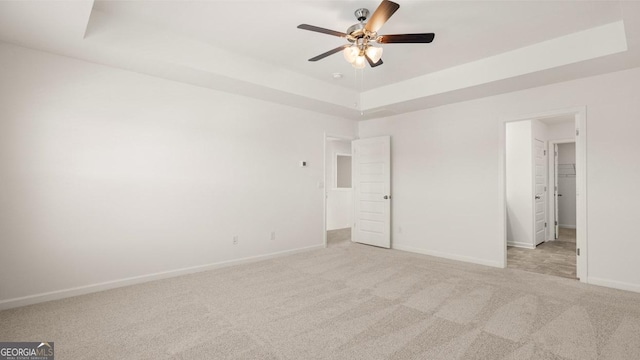 unfurnished bedroom with a raised ceiling, light colored carpet, and ceiling fan