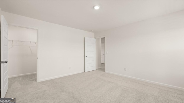 unfurnished bedroom with a spacious closet, light carpet, and a closet