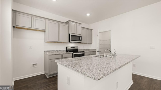 kitchen featuring sink, gray cabinets, stainless steel appliances, light stone counters, and a center island with sink