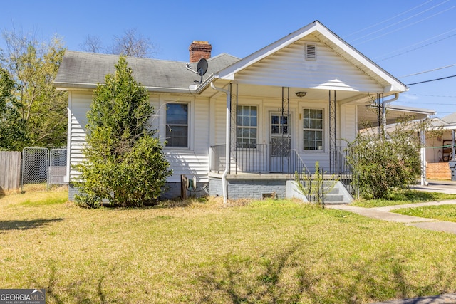 bungalow-style house with fence, a porch, roof with shingles, a front yard, and a chimney