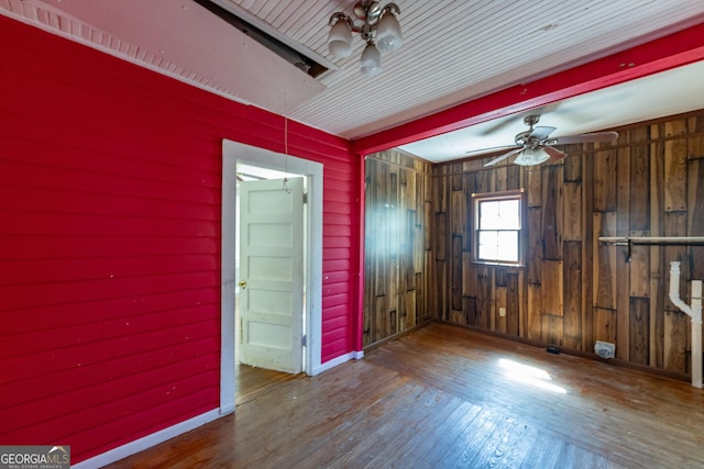 unfurnished room featuring wooden walls, baseboards, attic access, a ceiling fan, and wood-type flooring