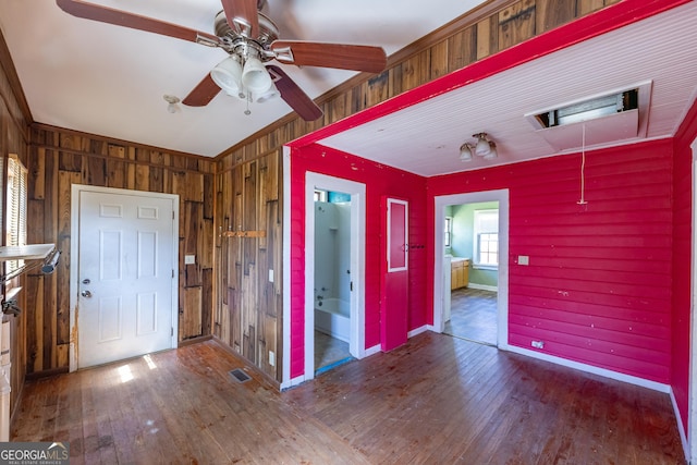 interior space with visible vents, hardwood / wood-style floors, wooden walls, baseboards, and ceiling fan