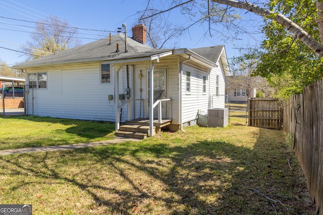 rear view of house with a shingled roof, a yard, fence, and a chimney