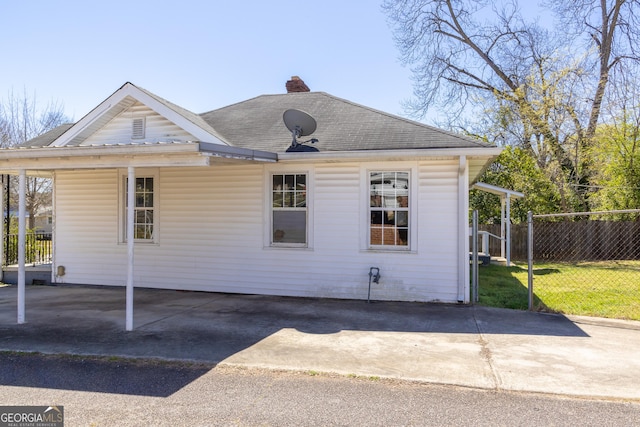 exterior space with fence, roof with shingles, a lawn, a chimney, and driveway