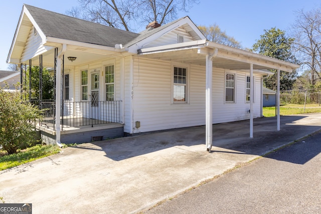 view of side of property featuring an attached carport, a porch, a chimney, and driveway