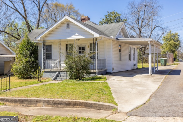 bungalow with a front lawn, a porch, concrete driveway, an attached carport, and a chimney