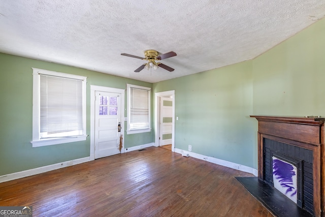unfurnished living room with a fireplace with raised hearth, ceiling fan, baseboards, wood finished floors, and a textured ceiling