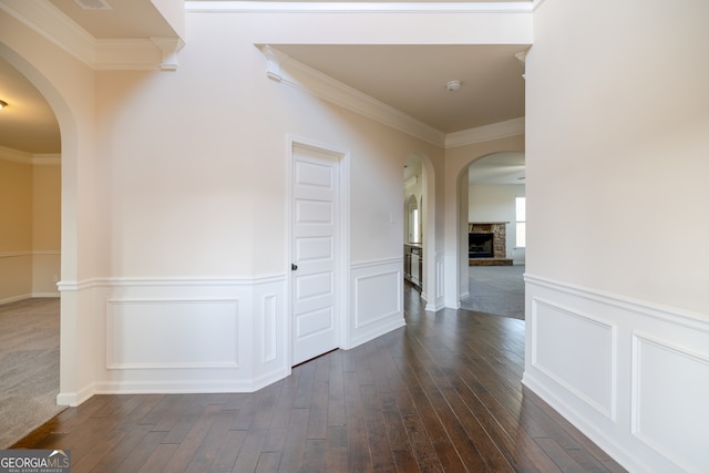 corridor with arched walkways, dark wood finished floors, a decorative wall, ornamental molding, and wainscoting